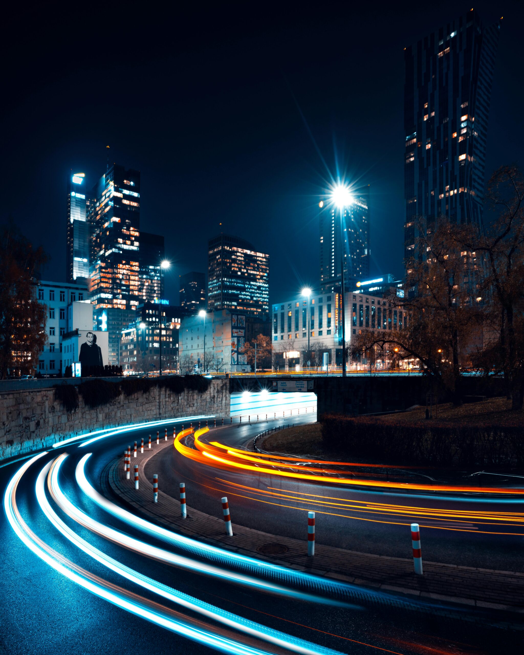 Long exposure of dynamic traffic lights against Warsaw's illuminated skyline at night.