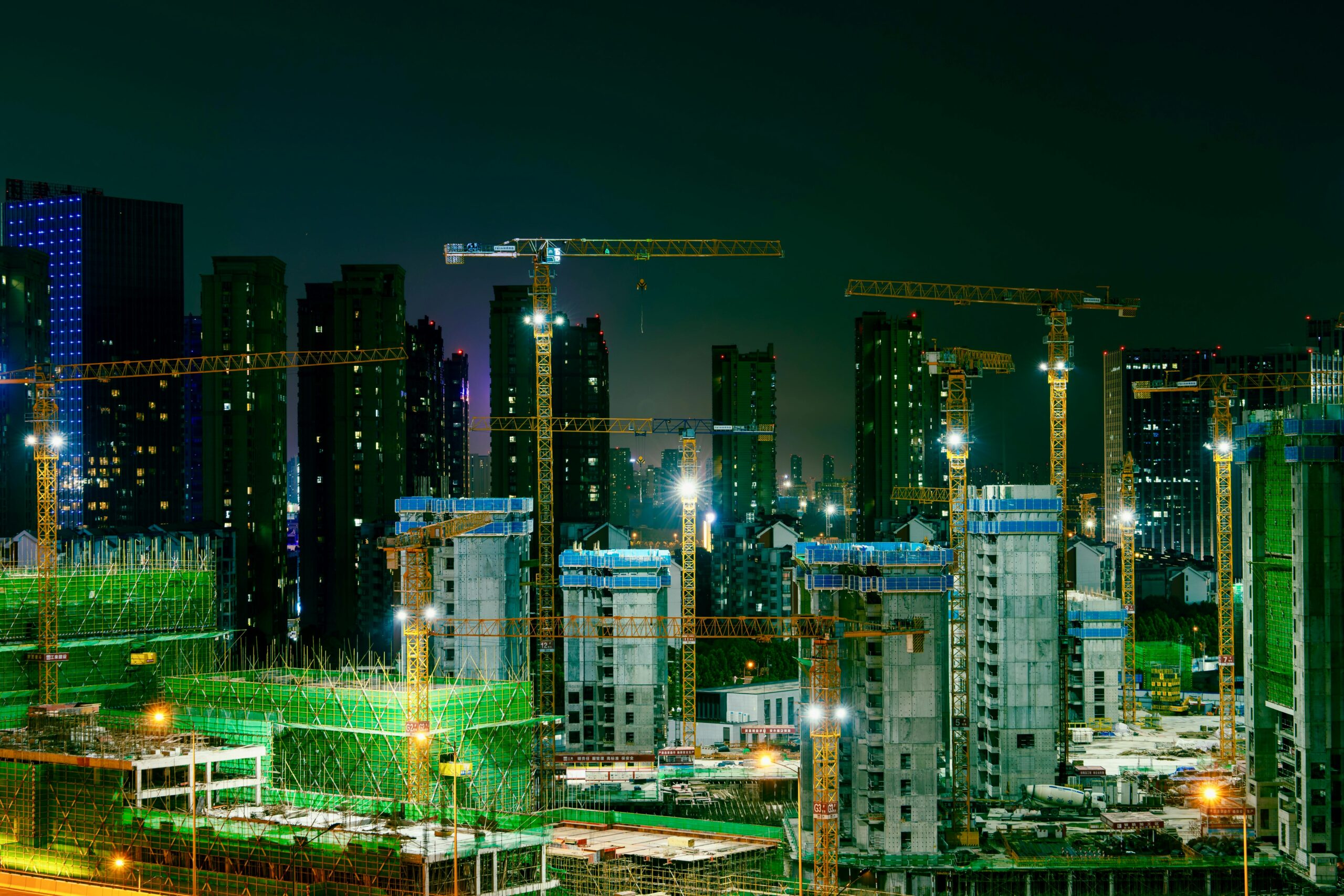Night view of a bustling construction site in an urban cityscape with cranes and high-rise buildings.